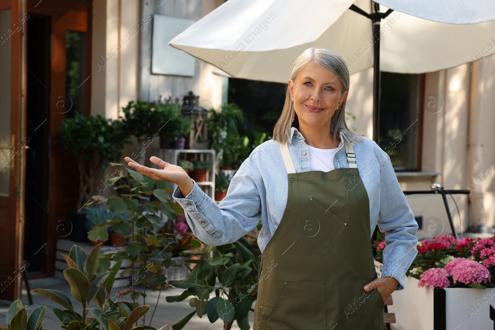 Photo of Happy business owner inviting to come into her flower shop outdoors, space for text