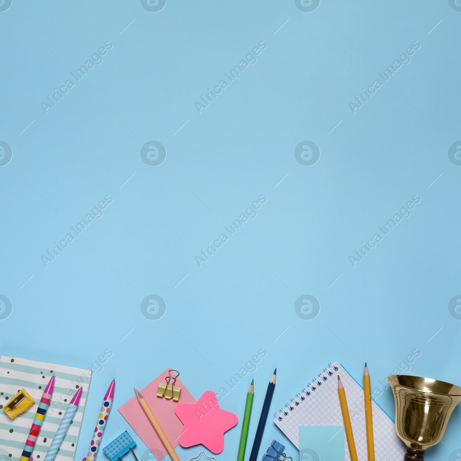 Image of Different stationery and school bell on light blue background, flat lay. Space for text