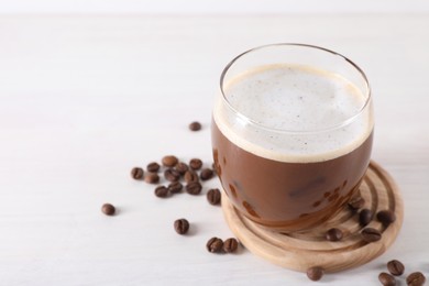 Photo of Refreshing iced coffee with milk in glass and beans on white table, closeup. Space for text