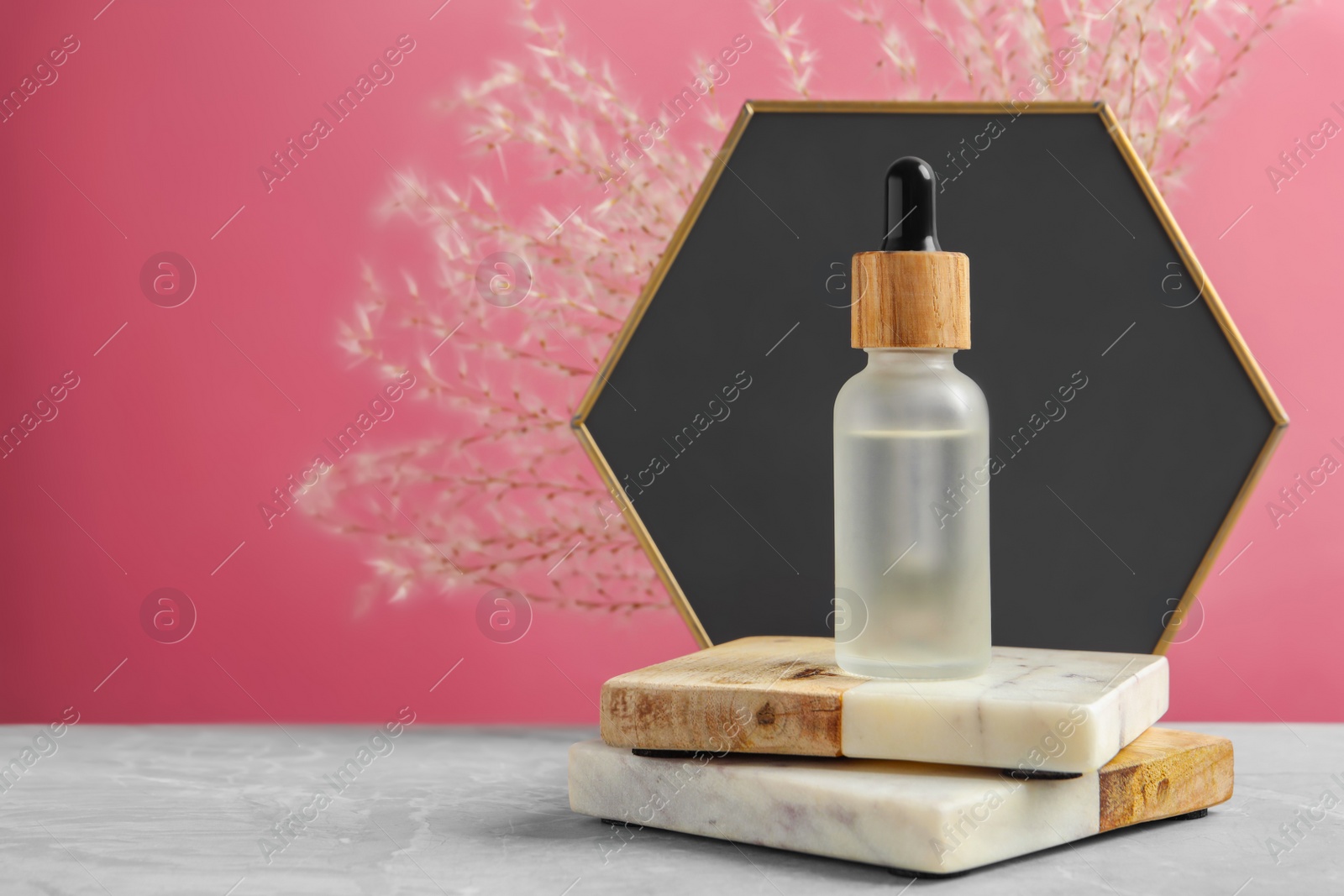 Photo of Bottle of face serum with marble boards on grey table against pink background. Space for text