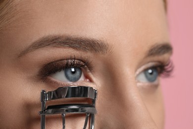 Photo of Young woman using eyelash curler on pink background, closeup