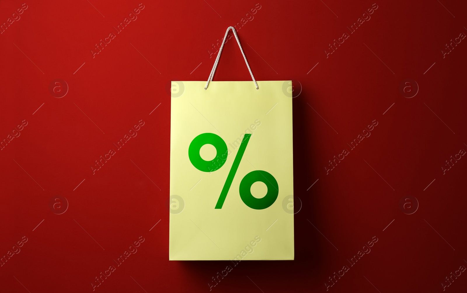 Image of Color paper shopping bag with percent sign hanging on red wall. Discount concept