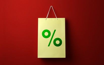 Image of Color paper shopping bag with percent sign hanging on red wall. Discount concept
