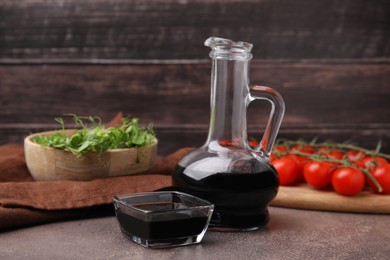 Photo of Organic balsamic vinegar, tomatoes and greens on grey table