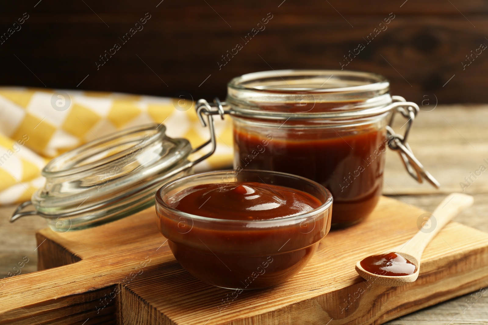 Photo of Tasty barbeque sauce in bowl, jar and spoon on wooden table, closeup