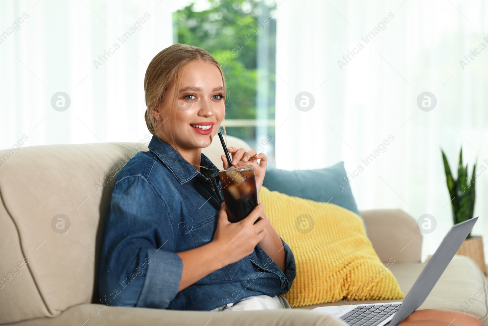 Photo of Young woman with glass of cola working on laptop at home. Refreshing drink