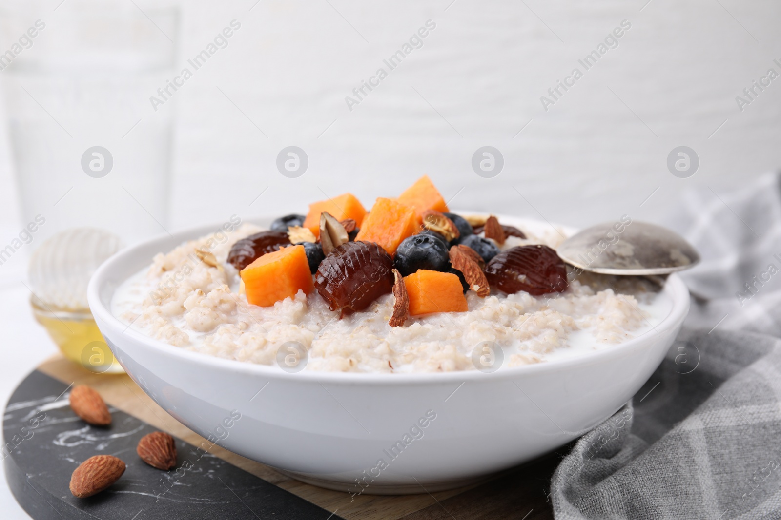 Photo of Delicious barley porridge with blueberries, pumpkin, dates and almonds in bowl on table, closeup