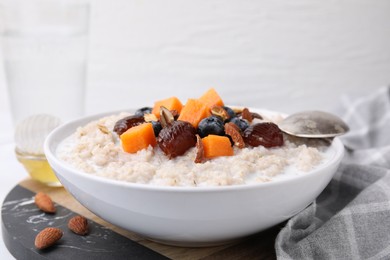 Photo of Delicious barley porridge with blueberries, pumpkin, dates and almonds in bowl on table, closeup