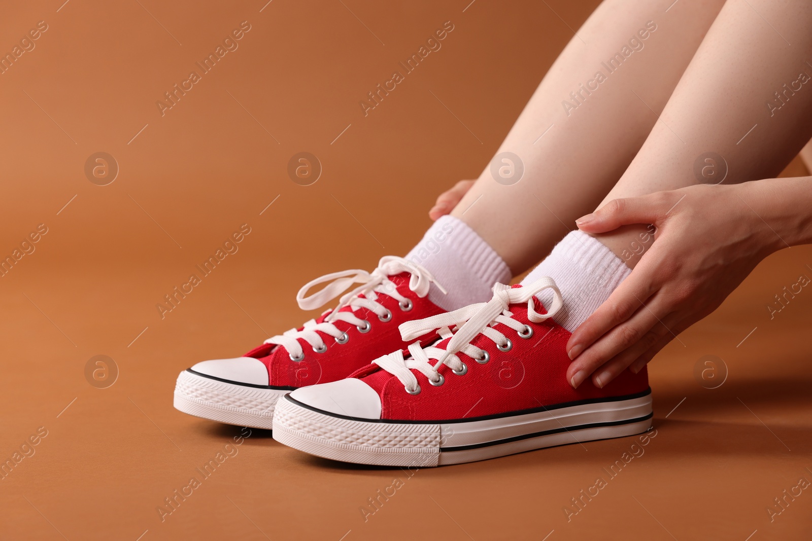 Photo of Woman wearing red classic old school sneakers on brown background, closeup