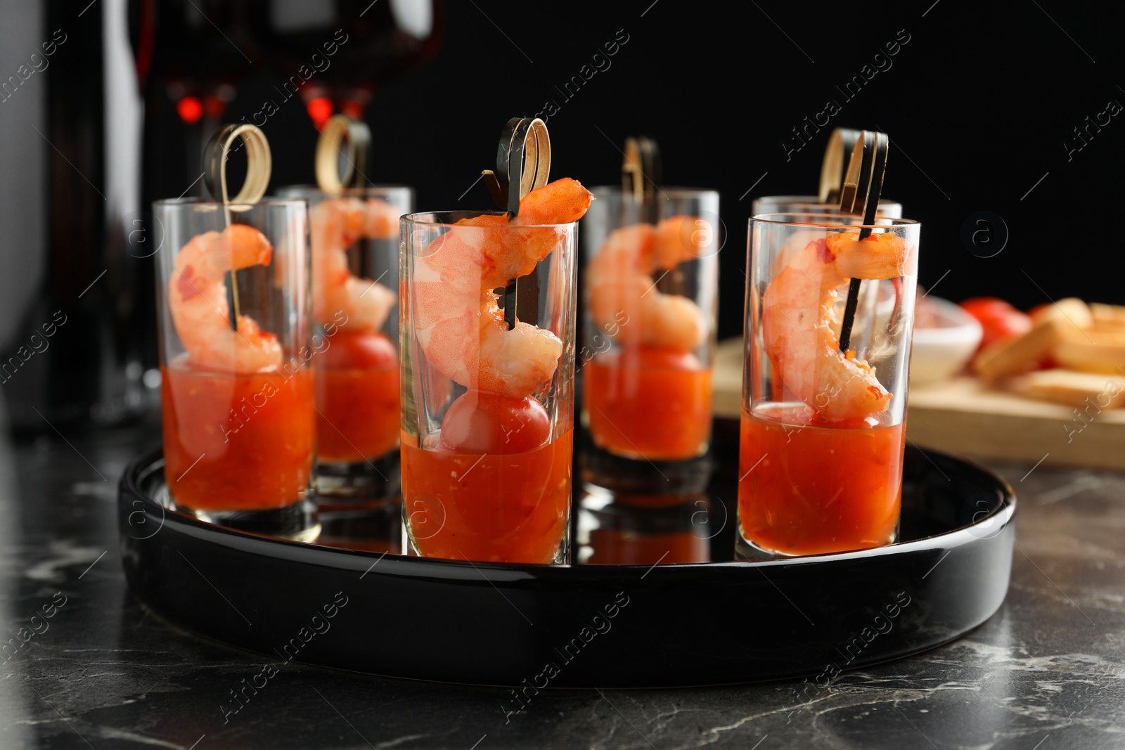 Photo of Tasty canapes with shrimps, tomatoes and sauce in shot glasses on black marble table, closeup