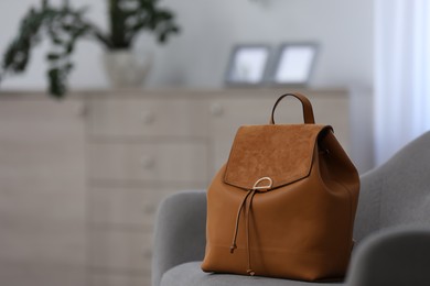 Stylish brown backpack on grey armchair indoors, space for text