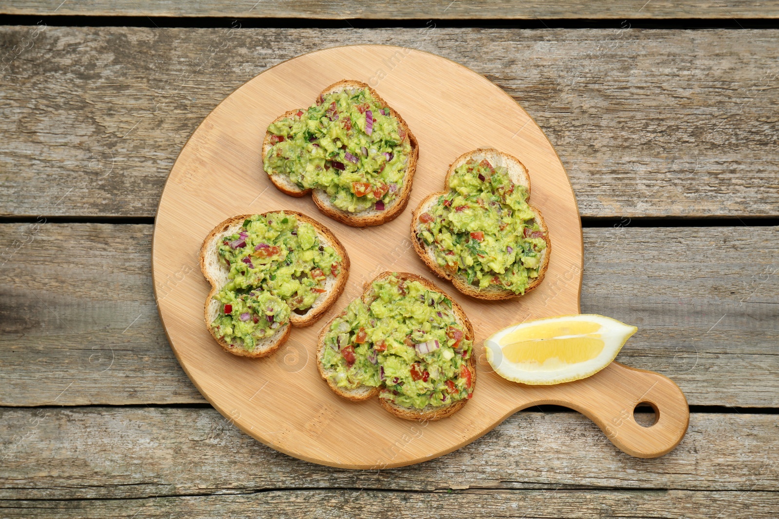 Photo of Slices of bread with tasty guacamole and lemon on wooden table, top view