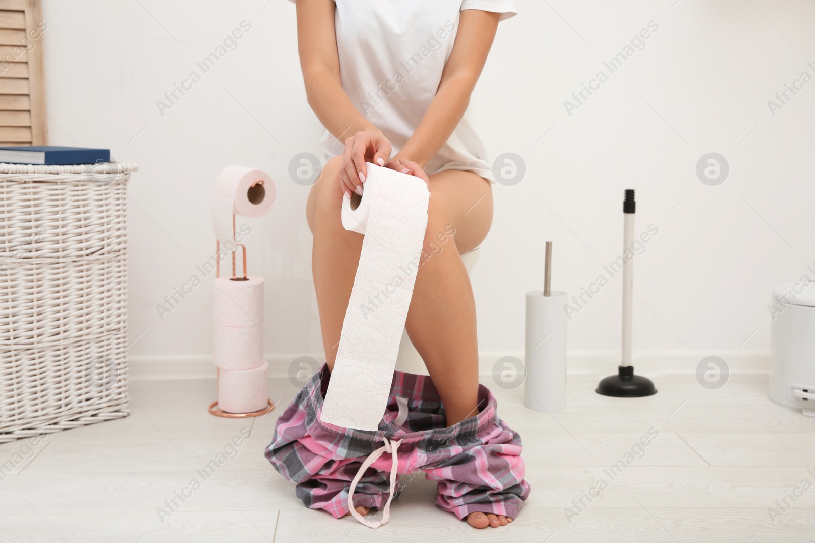 Photo of Young woman with paper roll sitting on toilet bowl in bathroom