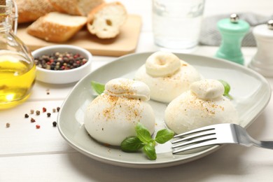 Delicious burrata cheese with basil on white wooden table, closeup