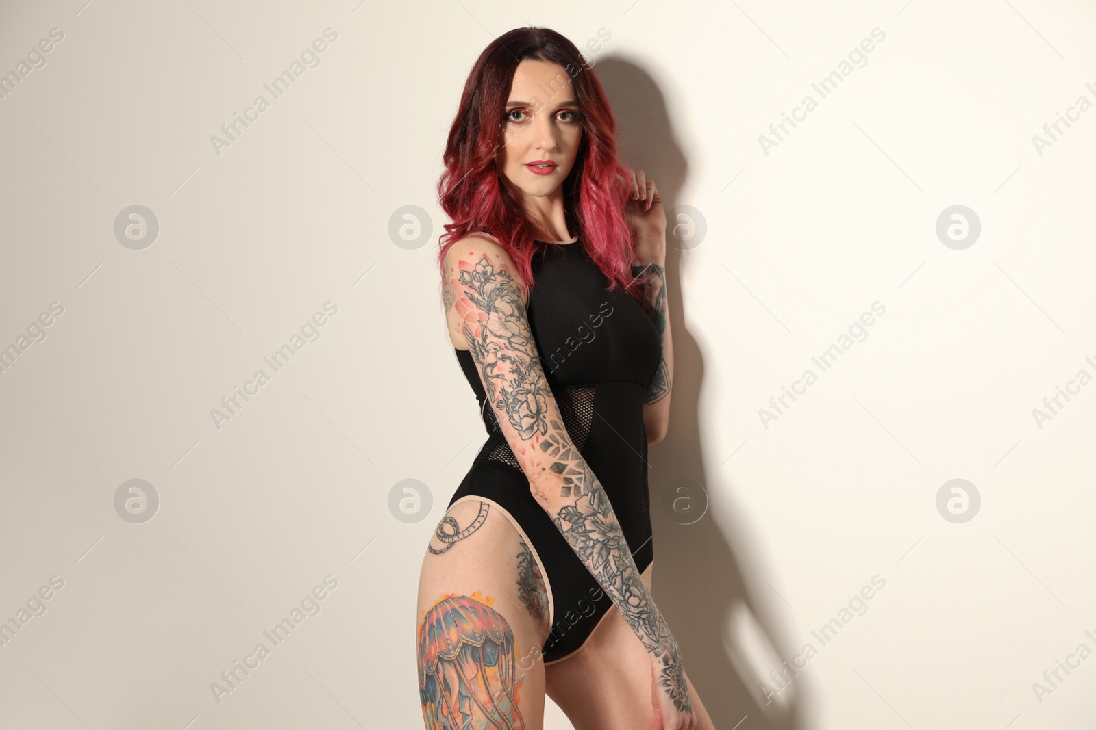 Photo of Beautiful woman with tattoos on body against light background