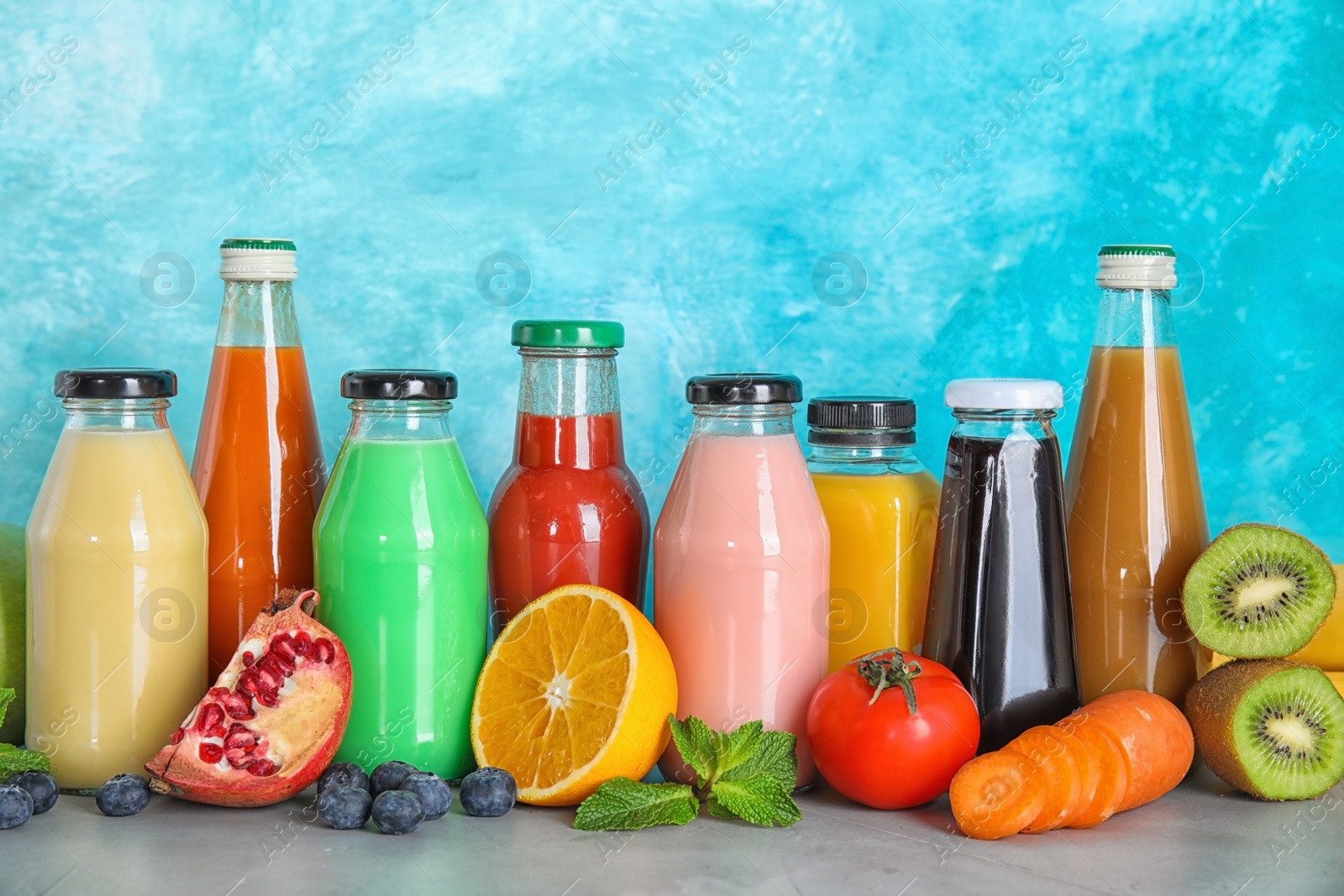 Photo of Bottles with different drinks and ingredients on table against color background