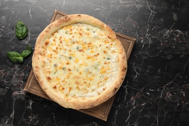 Photo of Delicious cheese pizza and basil on black marble table, flat lay