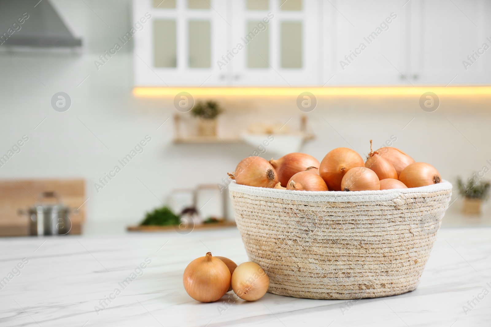 Photo of Basket with fresh onions on white marble table in modern kitchen. Space for text