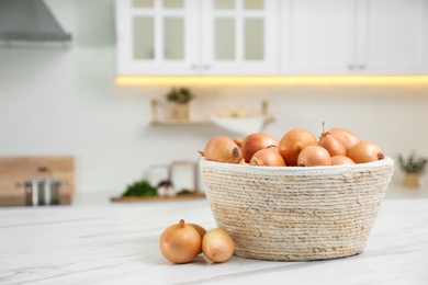 Photo of Basket with fresh onions on white marble table in modern kitchen. Space for text