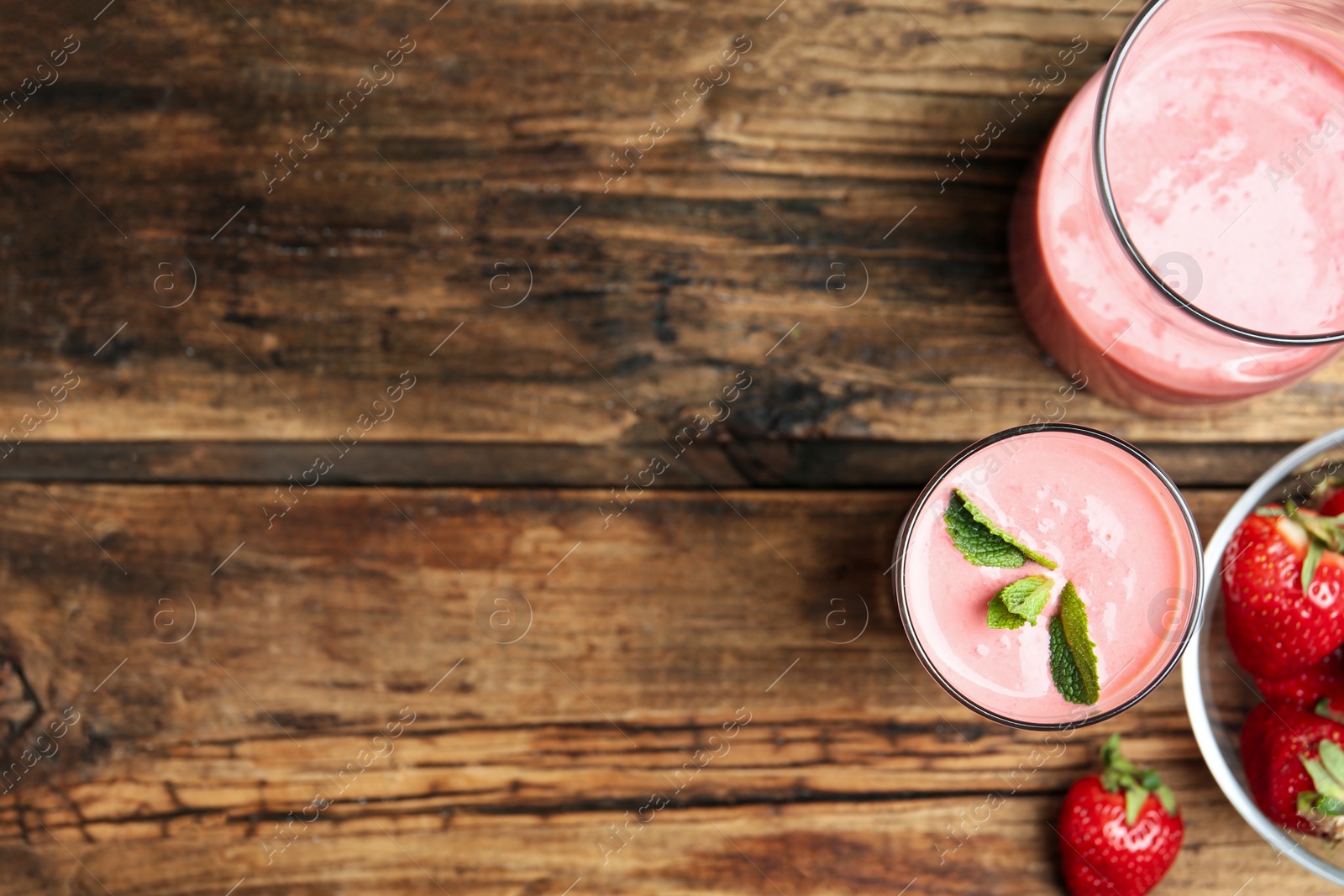 Photo of Tasty strawberry smoothies in glasses on wooden table, flat lay. Space for text