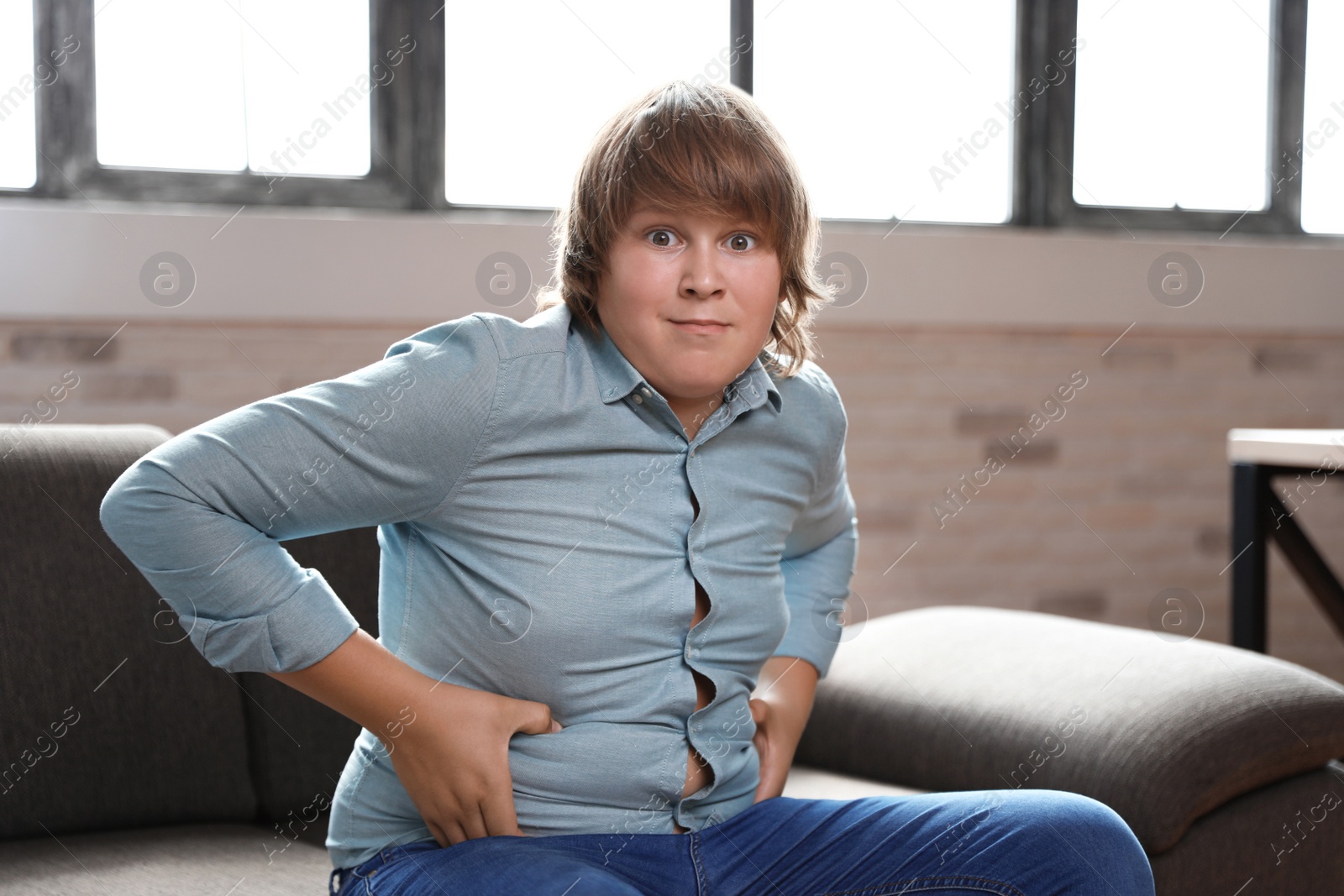 Photo of Emotional overweight boy sitting on sofa at home