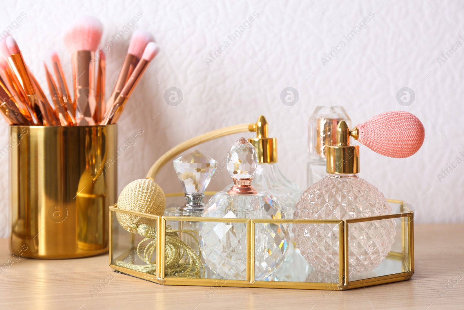 Photo of Luxury perfumes and makeup brushes on wooden dressing table
