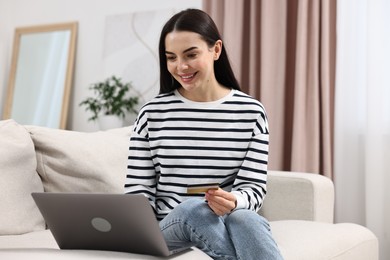 Photo of Happy young woman with credit card and laptop shopping online at home