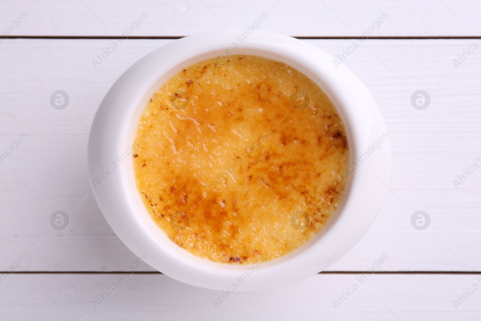 Photo of Delicious creme brulee in bowl on white wooden table, top view