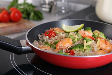 Photo of Tasty rice with shrimps and vegetables in frying pan on induction stove, closeup