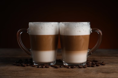 Photo of Glass cups of delicious layered coffee and beans on wooden table against dark background