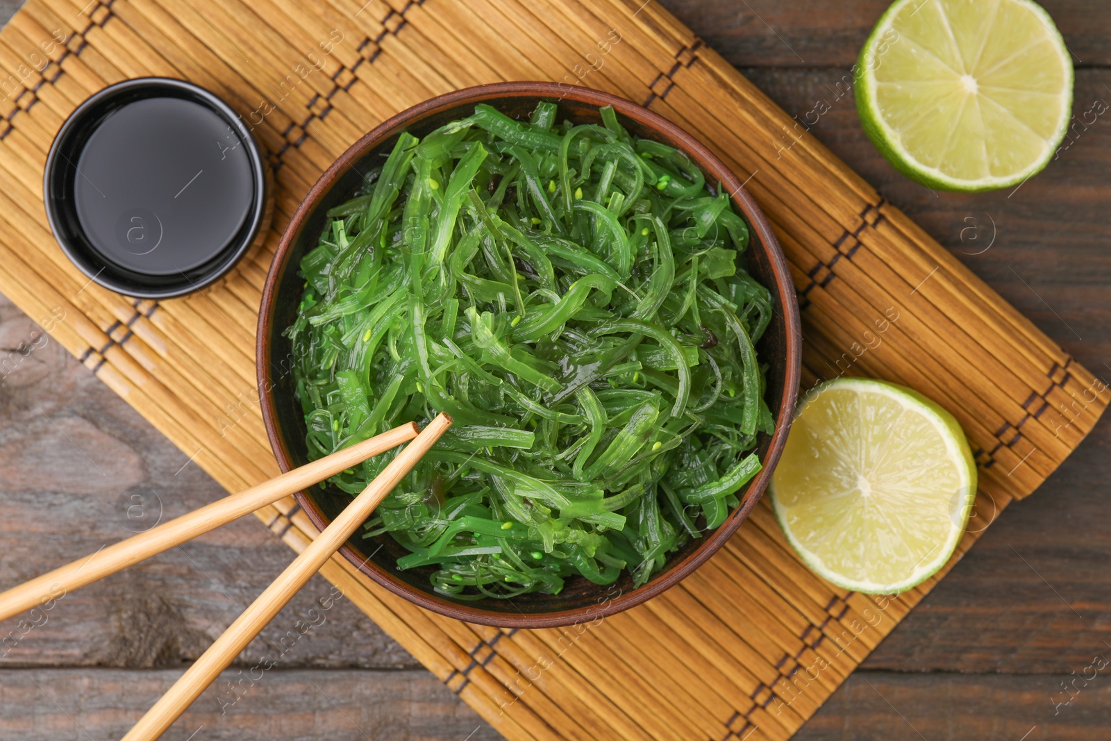 Photo of Tasty seaweed salad in bowl served on wooden table, flat lay