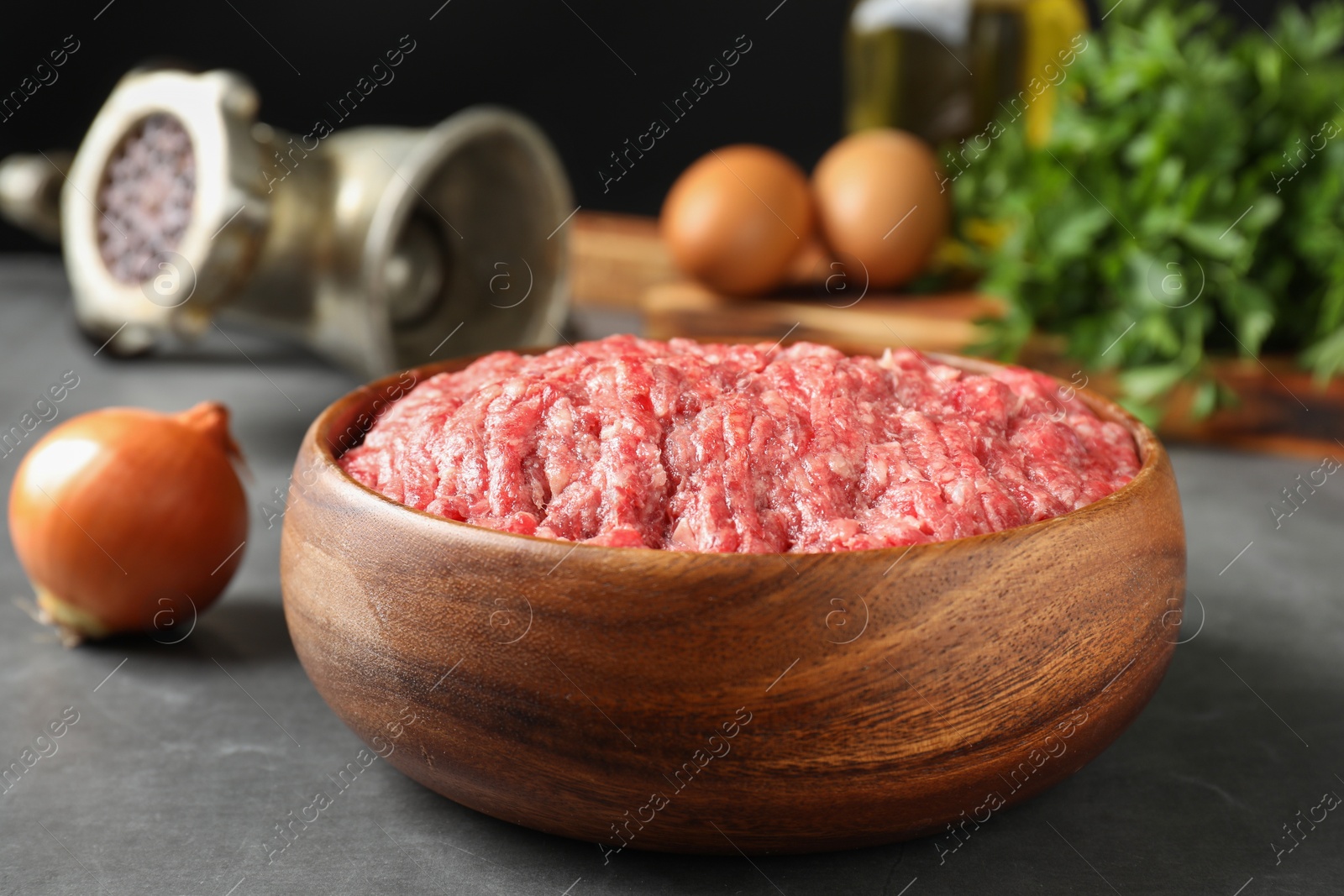 Photo of Raw ground meat in bowl and onion on grey table, closeup