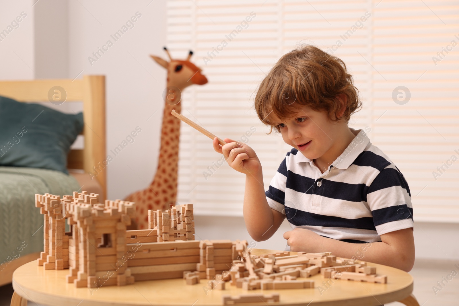 Photo of Cute little boy playing with wooden construction set at table in room. Child's toy