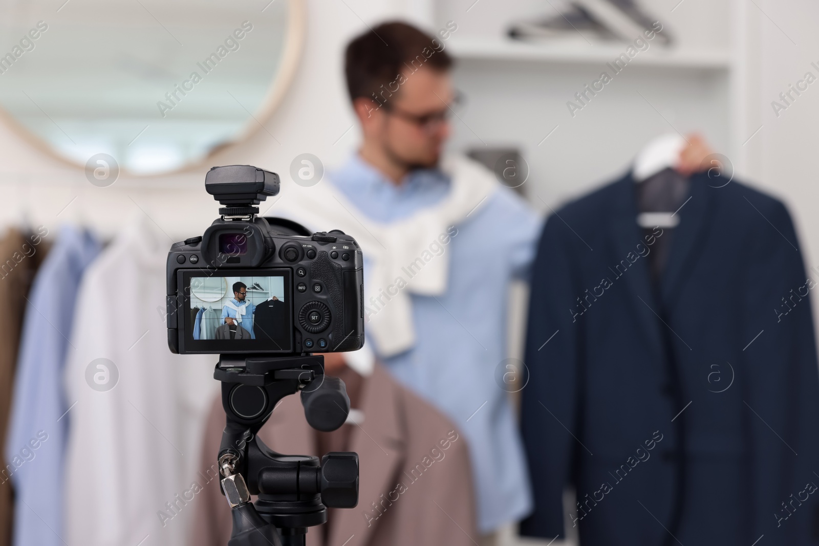 Photo of Fashion blogger showing clothes while recording video at home, focus on camera