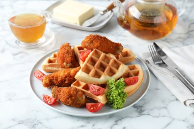 Tasty Belgian waffles served with fried chicken, tomatoes, lettuce and tea on white marble table