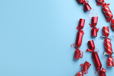 Photo of Red Christmas crackers with shiny confetti on light blue background, flat lay. Space for text