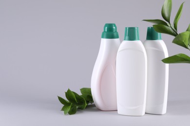 Photo of Bottles of cleaning product and green leaves on light background. Space for text