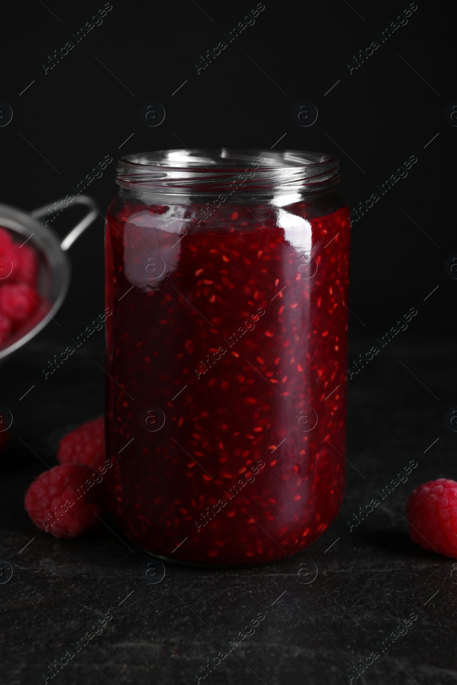 Photo of Delicious jam and fresh raspberries on black slate table, closeup