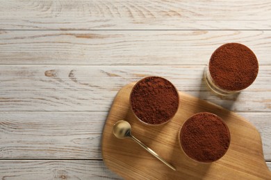 Photo of Delicious tiramisu in glasses and spoon on light wooden table, top view. Space for text