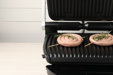 Photo of Electric grill with homemade sausages and rosemary on wooden table. Space for text