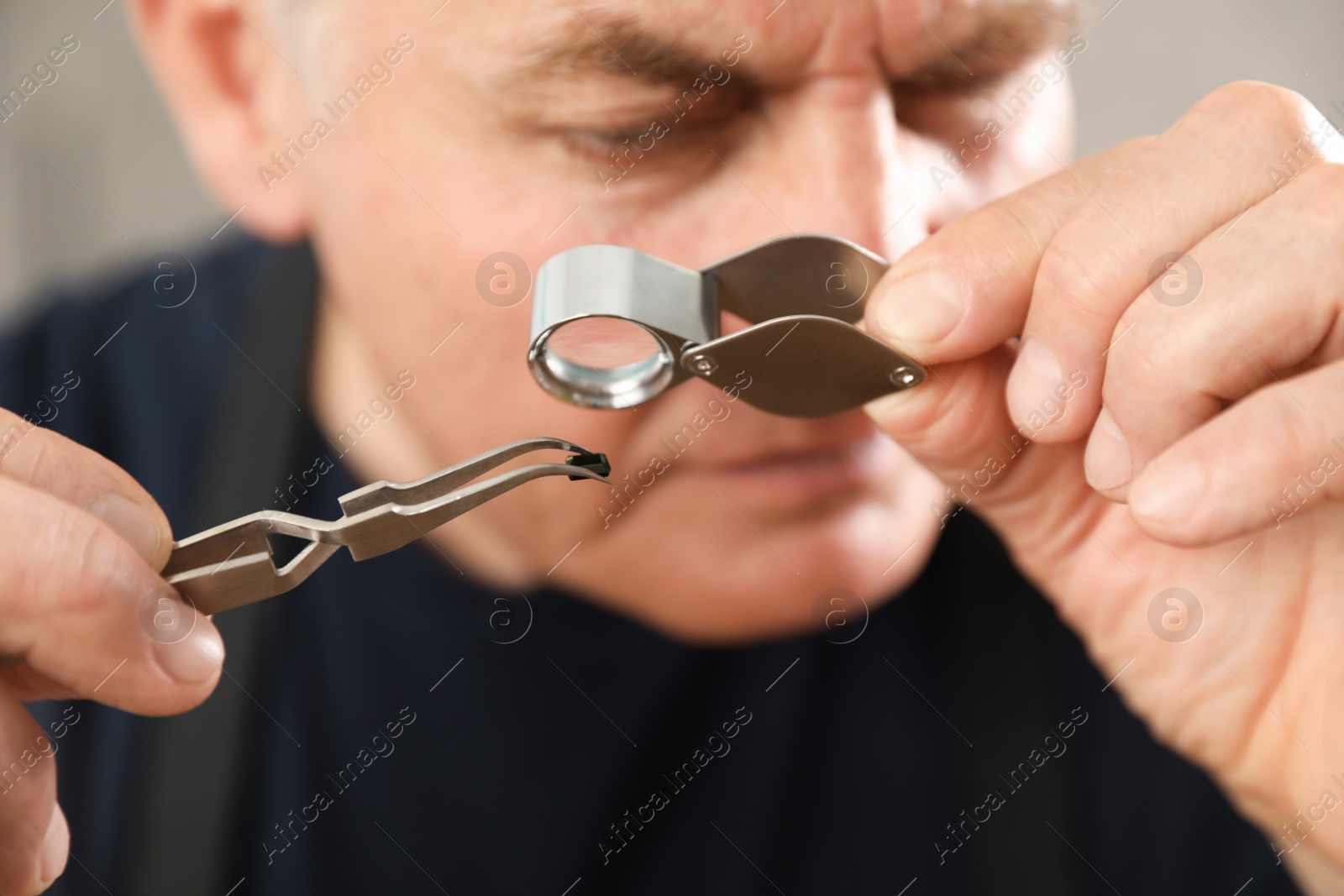 Photo of Male jeweler evaluating precious gemstone in workshop, closeup