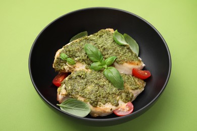 Delicious chicken breasts with pesto sauce, tomatoes and basil on light green table, closeup