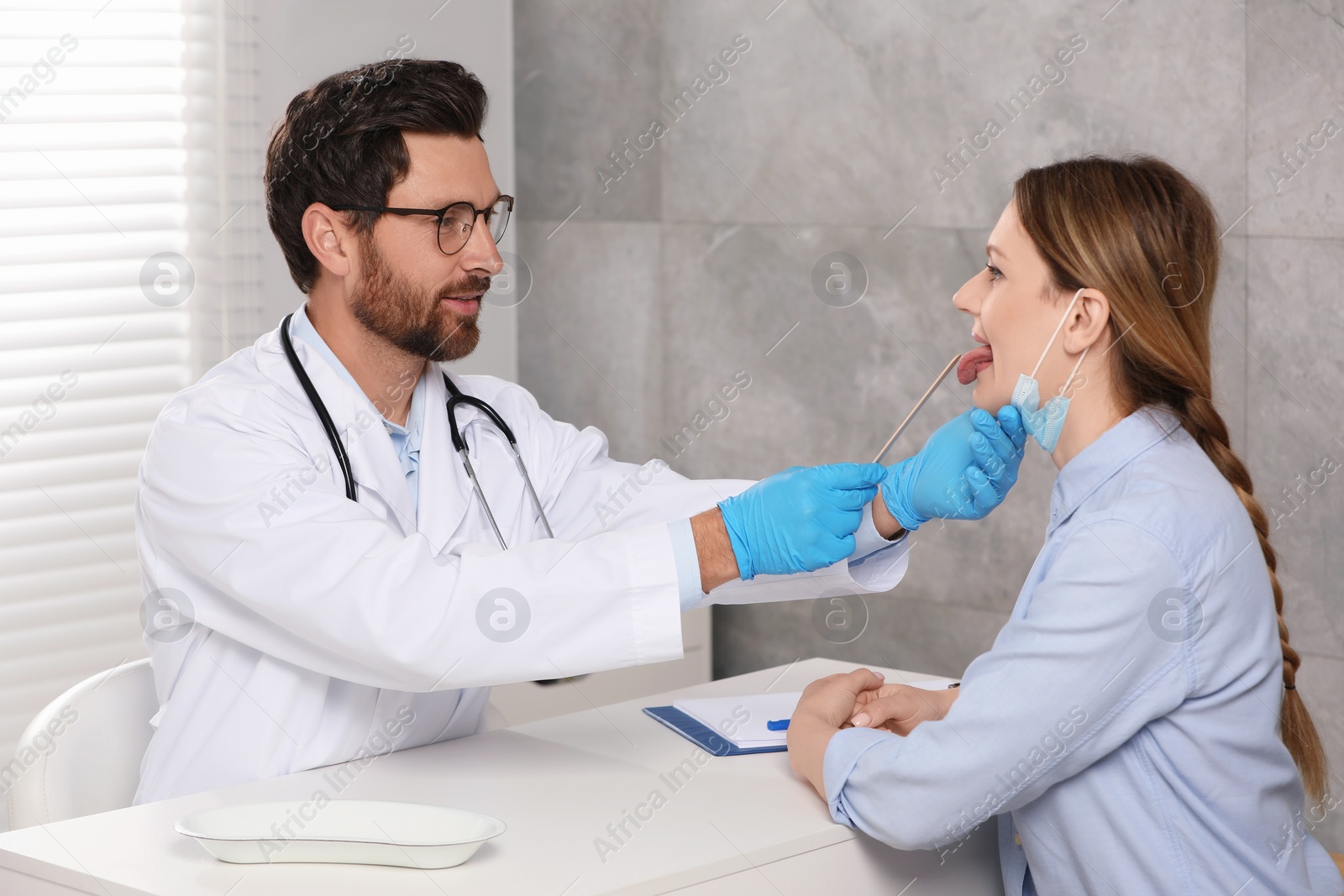 Photo of Doctor examining woman`s oral cavity with tongue depressor in hospital