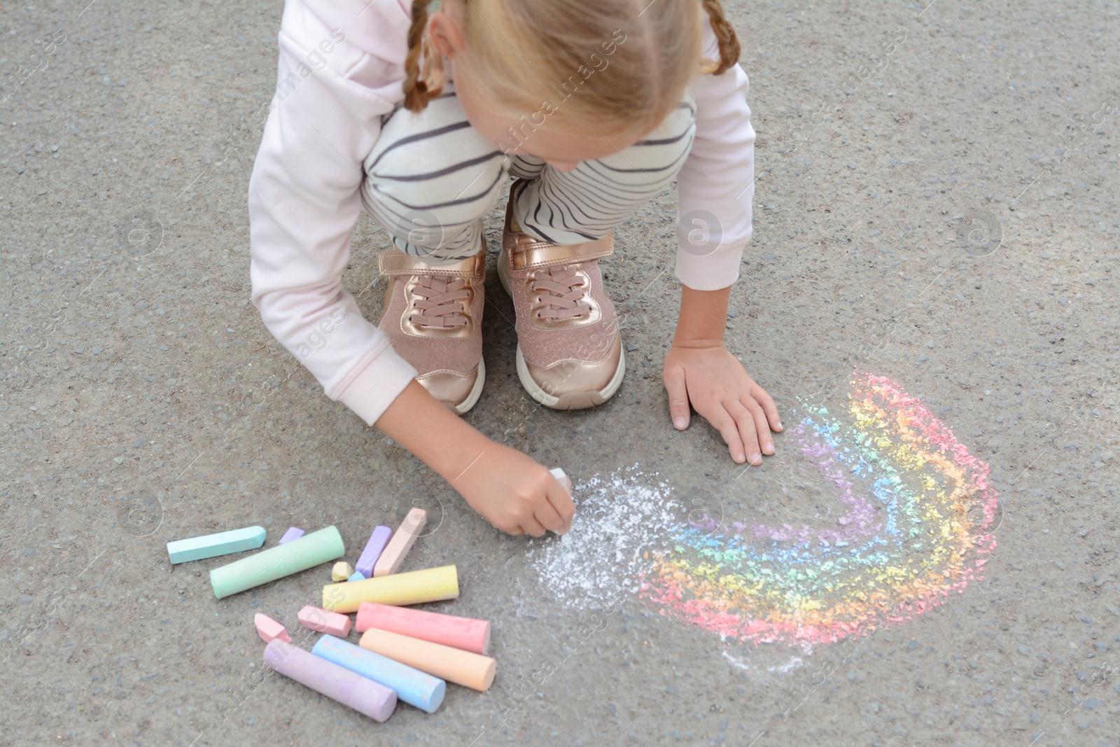 Photo of Little child drawing rainbow with chalk on asphalt