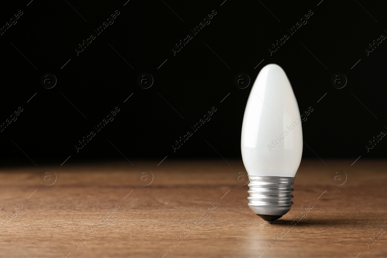 Photo of New modern lamp bulb on wooden table against black background. Space for text