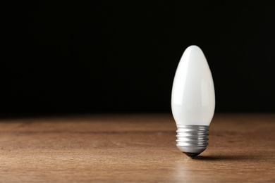 New modern lamp bulb on wooden table against black background. Space for text