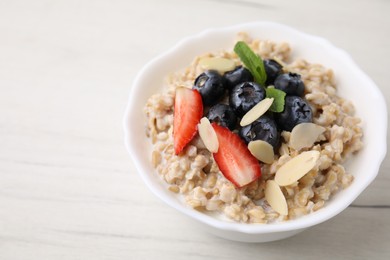 Photo of Tasty oatmeal with strawberries, blueberries and almond petals in bowl on white wooden table, closeup. Space for text