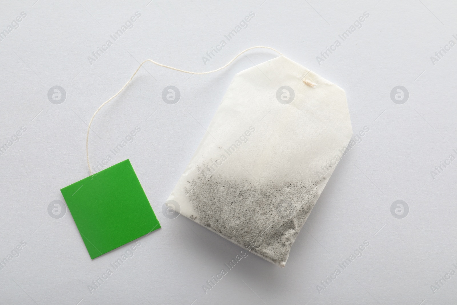 Photo of Unused tea bag with tag on white background, top view. Space for text