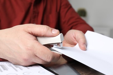 Photo of Man with papers using stapler at table, closeup