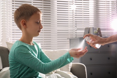 Photo of Mother spraying sanitizer on her son's hands at home